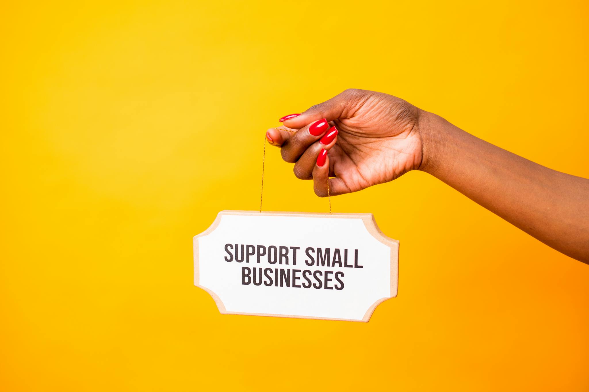 Hand holding a 'Support Small Businesses' sign against a vibrant yellow background, promoting local commerce.
